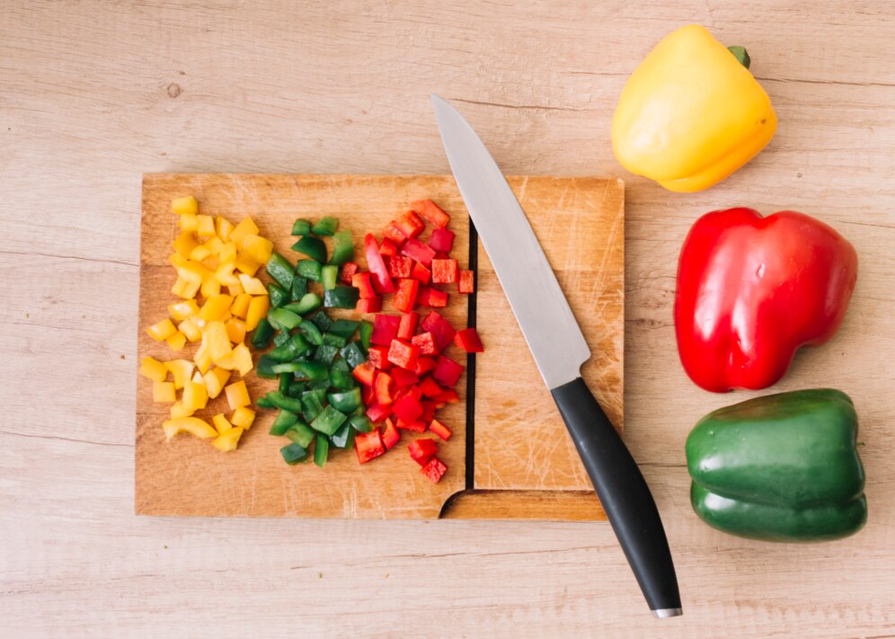 whole-chopped-red-green-yellow-bell-peppers-chopping-board-with-sharp-knife-against-wooden-backdrop_23-2148082918